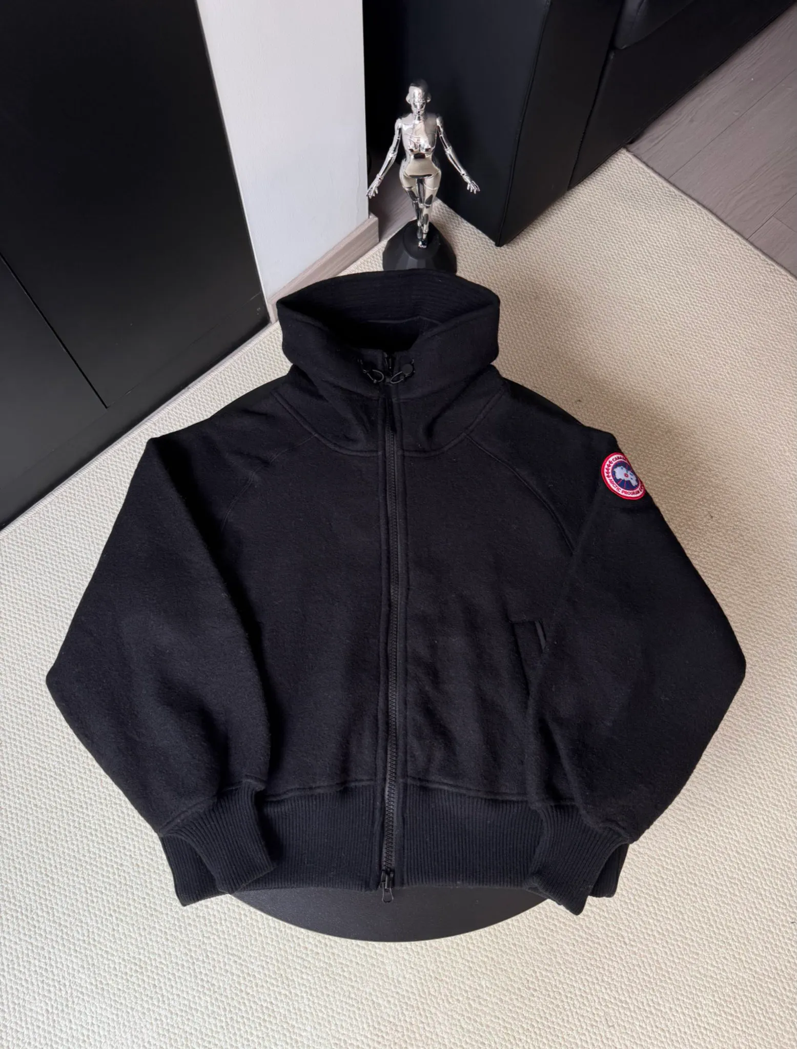 P660 Canada Goose Fleece Wool Badge Hooded Jacket Fabric selection: Wool fleece fabric blended with wool as the main body and a very small amount of spandex and polyester fiber. Wool is a core natural ingredient that provides unparalleled temperature regulation, antibacterial and anti-odor properties and a skin-friendly feel. The feeding of a small amount of spandex gives the fabric a certain degree of four-way elasticity, making it non-restrictive during daily activities. As the basis of fleece's structure, polyester fiber enhances the fabric's durability, wrinkle resistance and quick-drying properties. It contributes to the loft of the fleece and provides functions such as trapping air.  Detail 1: The sleeves and hem are closed with 2×2 ribbing. Its strong elasticity can closely fit wrists and waists of different thicknesses, forming an effective 'seal' to prevent cold wind from blowing back. It can still maintain its original shape after repeated stretching and use, and is not easy to loose and deform. And the ribbed cuffs can convey a sense of design and enhance the visual beauty.  Detail 2: The combination of hood design and elastic buckle improves warmth and windproof performance when wearing. Accessories: Customized elastic drawstring, elastic buckle, custom zipper pendant, custom armband Size: S M L Color: black gray coffee rice pink